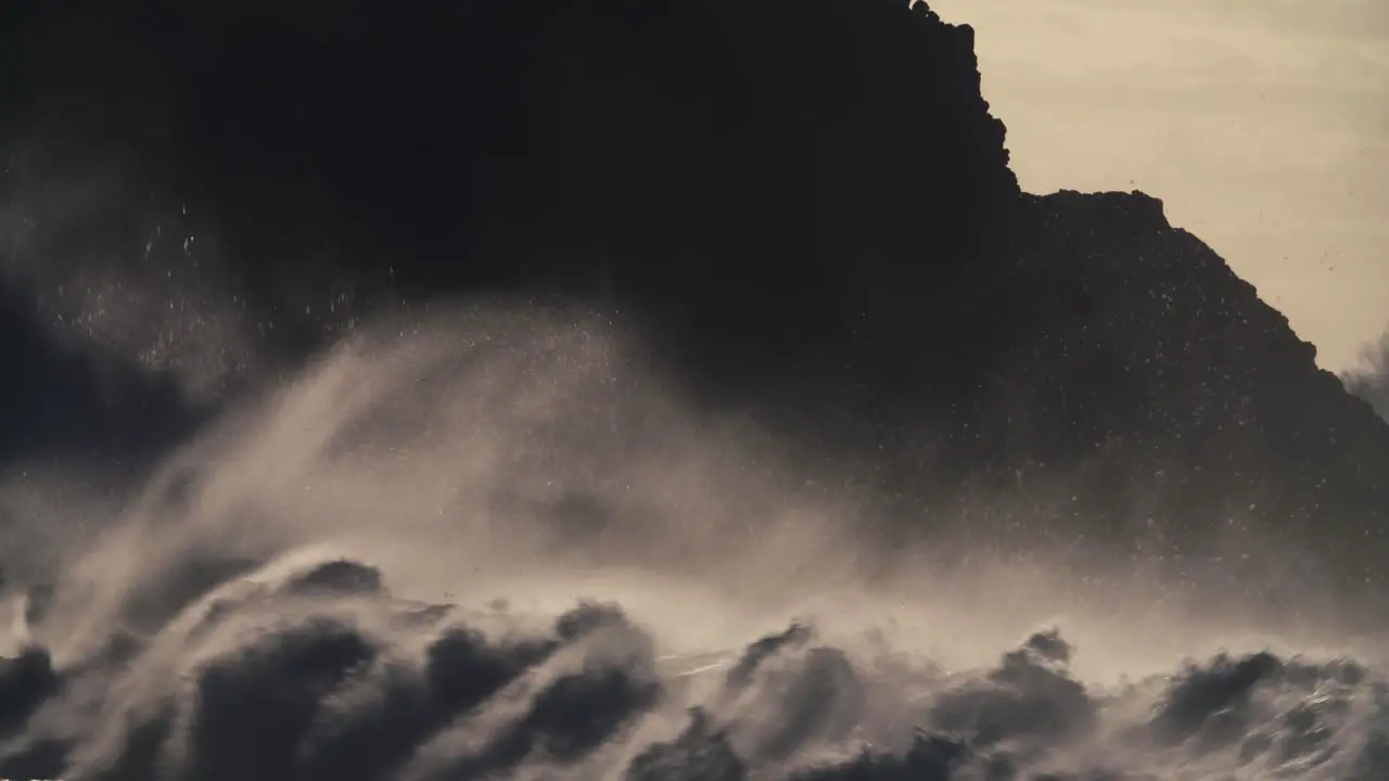 Huge ocean waves roll into a rocky shore in slow motion