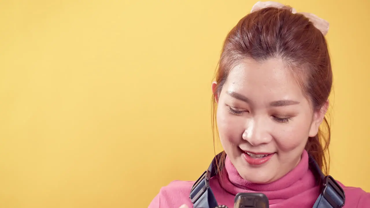 Asian gorgeous young woman in a studio shot over an isolated yellow background using a digital camera for travel and technology concept