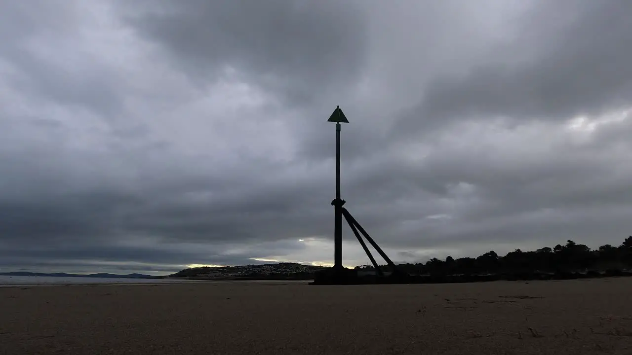 Overcast stormy clouds pass above metal high tide marker on sandy beach coastline timelapse