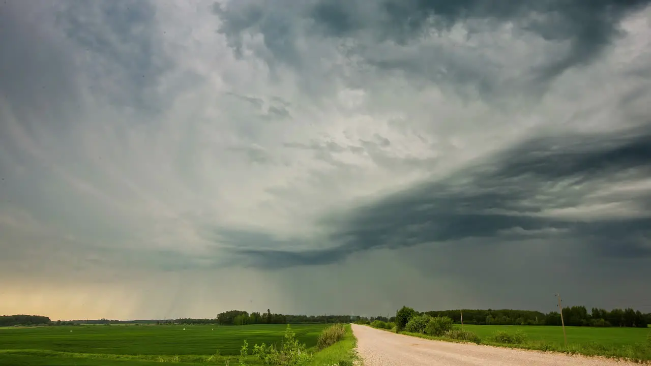 Dark rain clouds over country road and green field dramatic timelapse