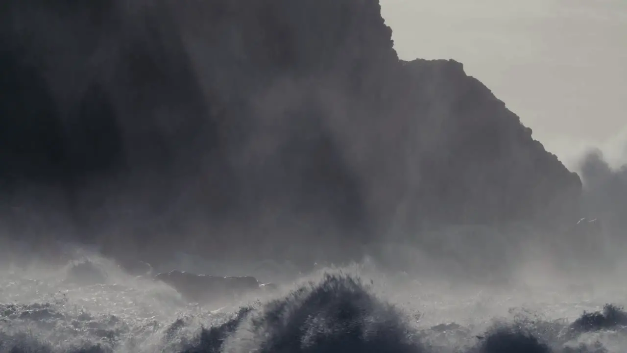 Huge ocean waves roll and crash into a rocky shore in slow motion 2