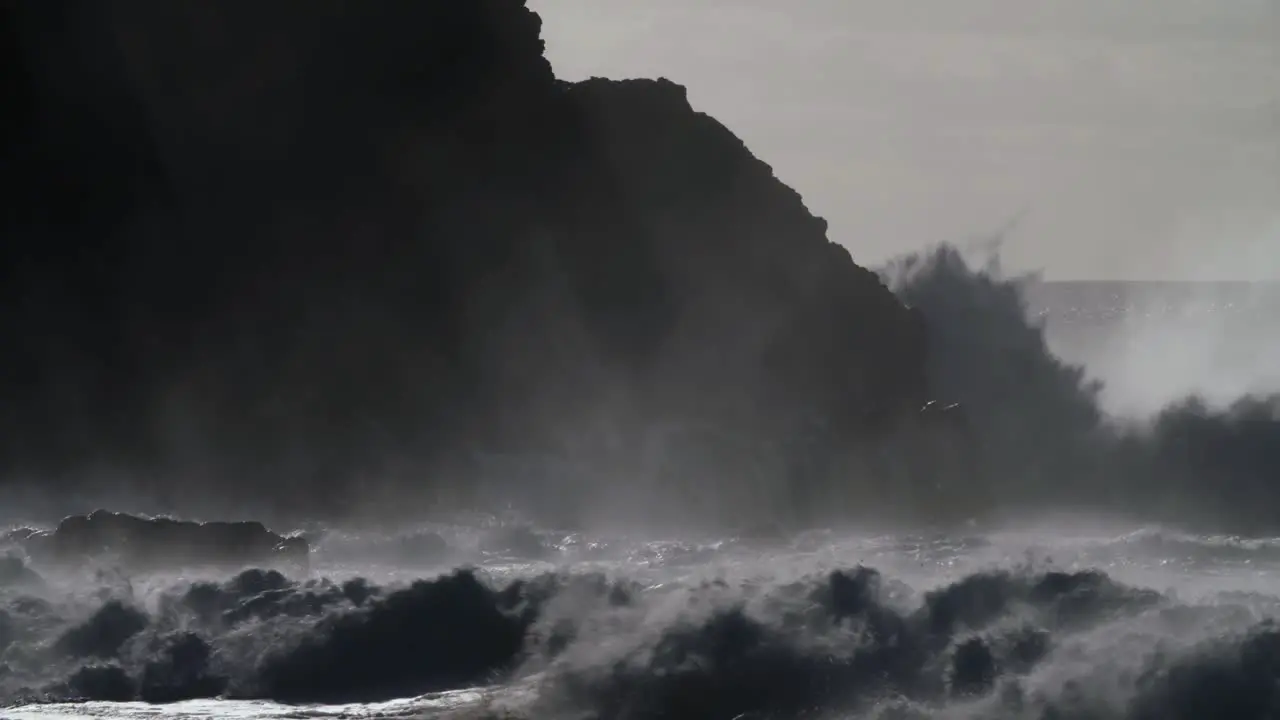 Huge ocean waves roll and crash into a rocky shore in slow motion