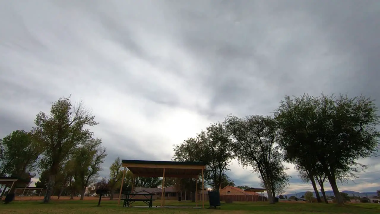 Timelapse of wispy grey clouds over park pavilion with brief rainbow