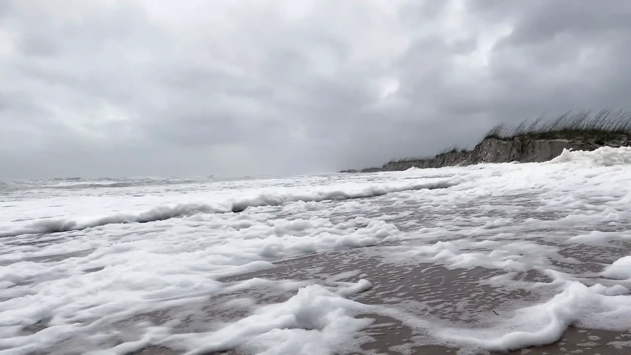 Wind blows sea foam across beach into dunes as Hurricane Nicole comes ashore