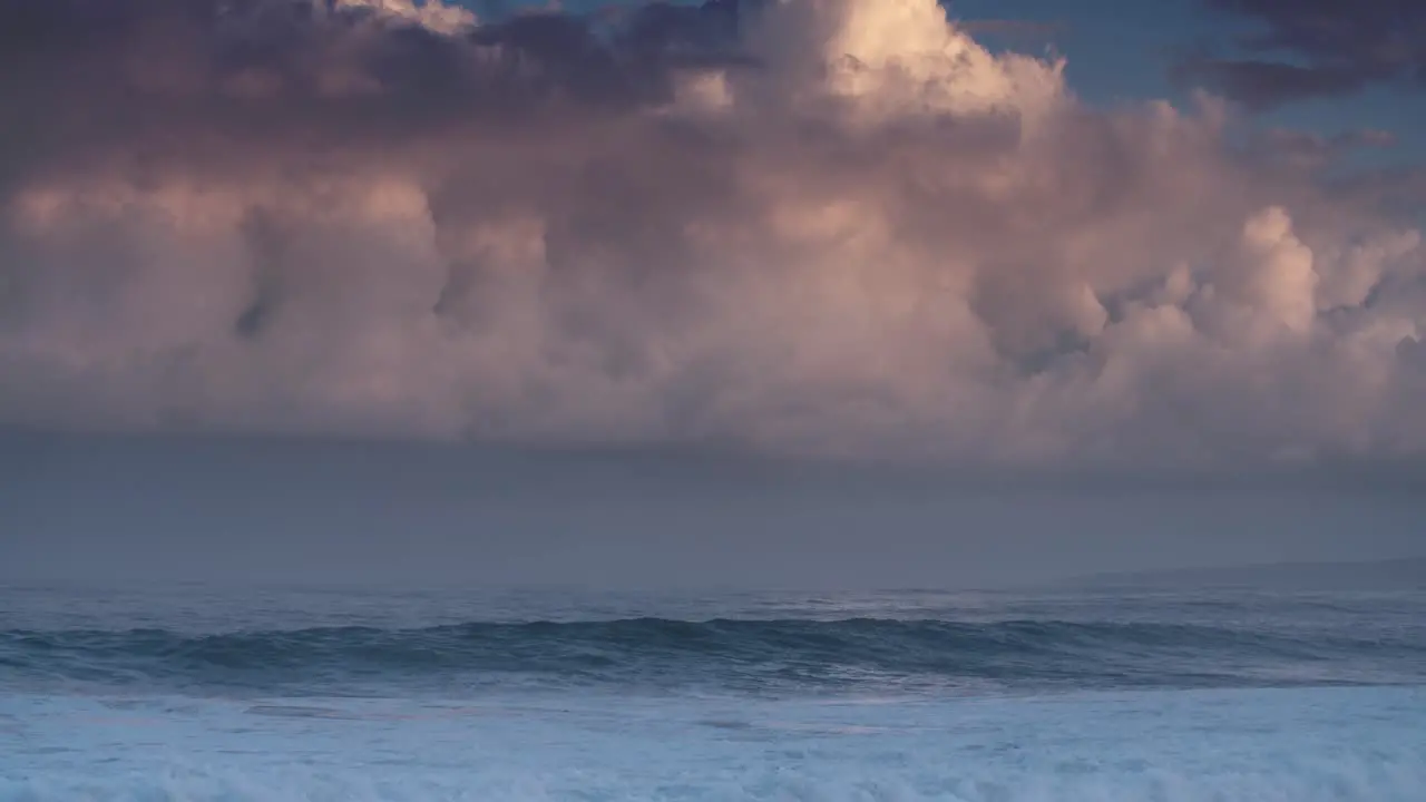 Blue waves roll into the coast of Hawaii in slow motion with pink clouds background