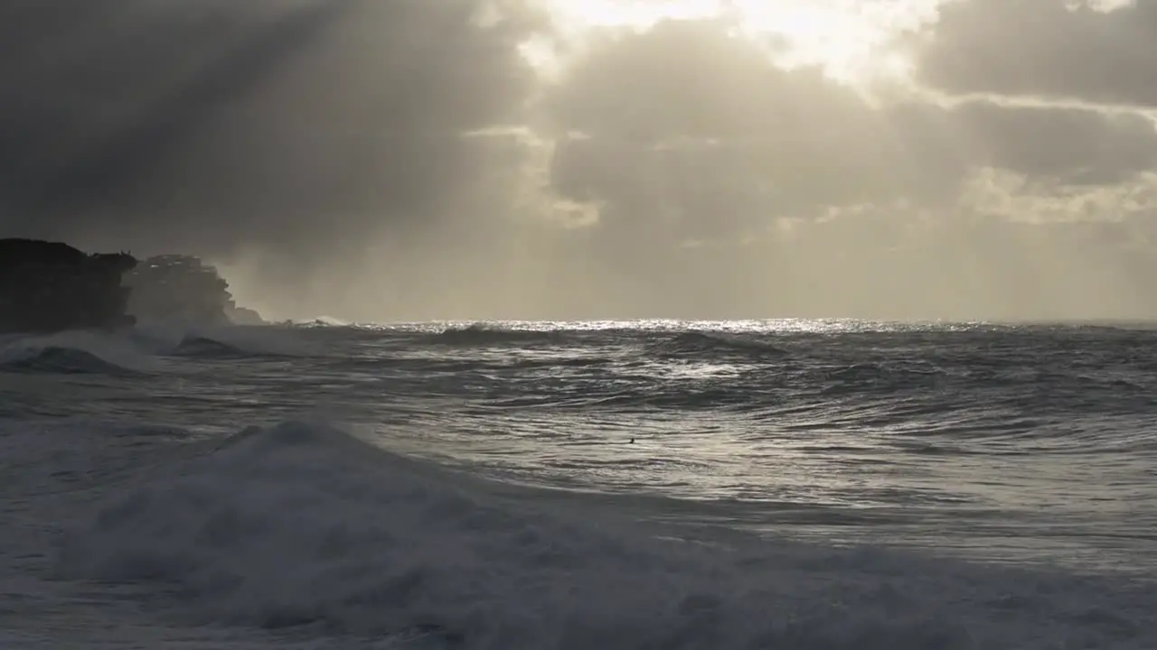 Unrecognisable lone surfer centre of screen paddling out during stormy sunrise at Bronte Beach Sydney