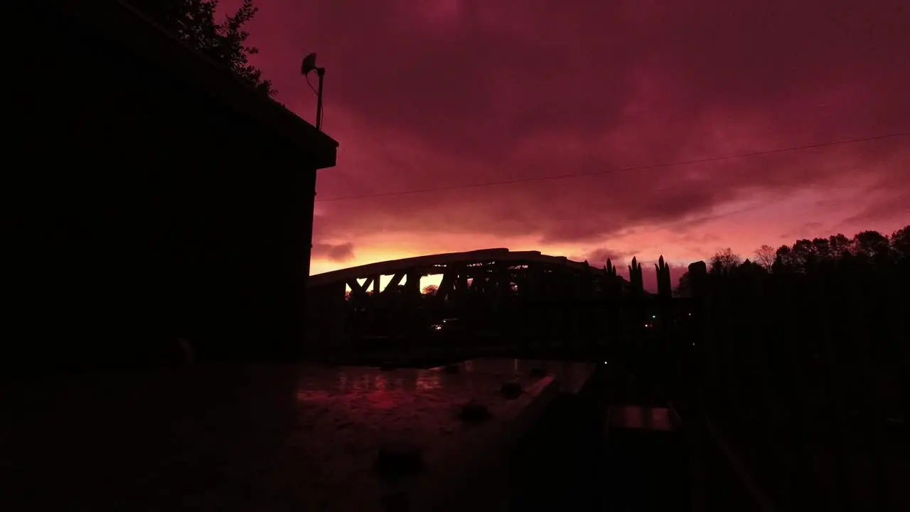 Red sunrise cloudy sky time lapse passing above arched canal bridge silhouette