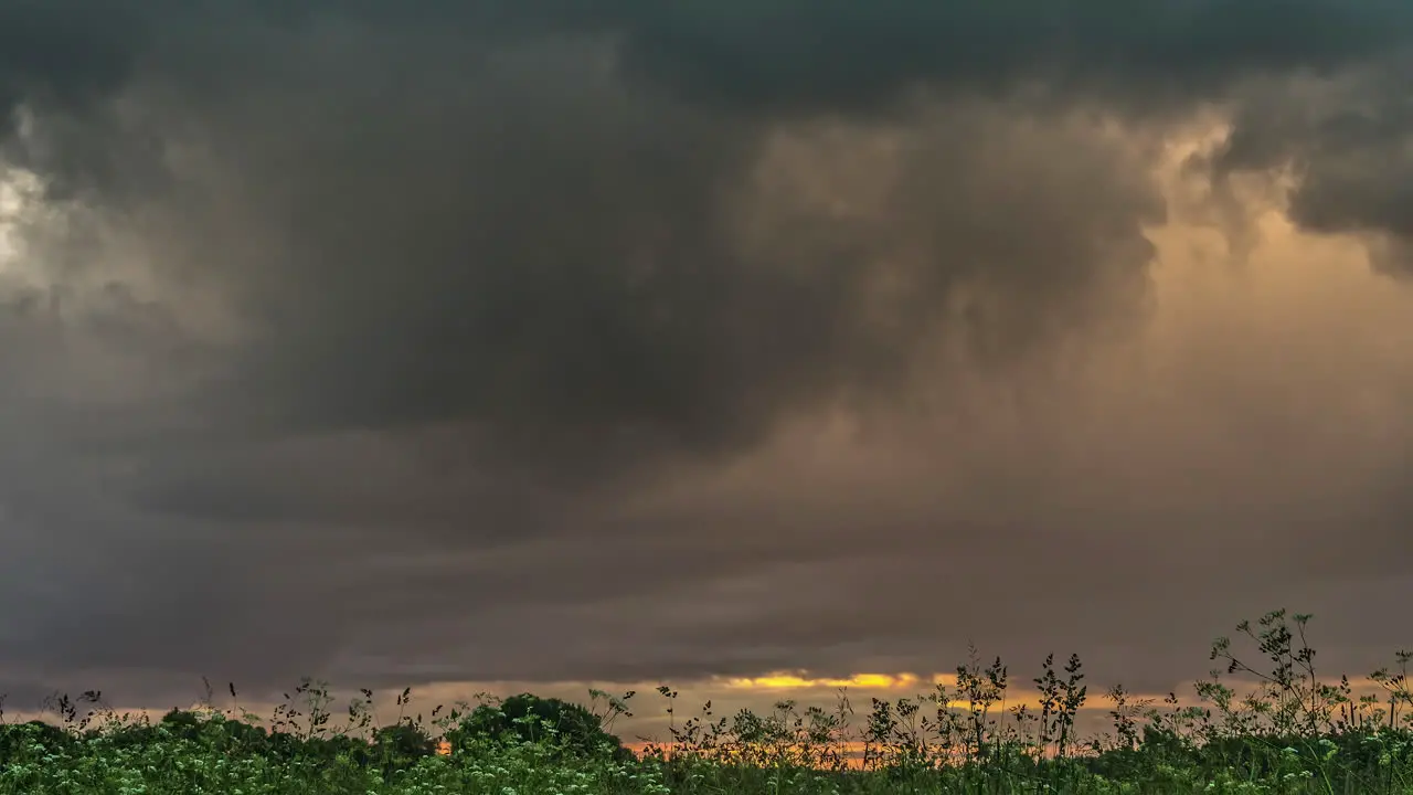 Dark stormy clouds flowing above meadow landscape fusion time lapse