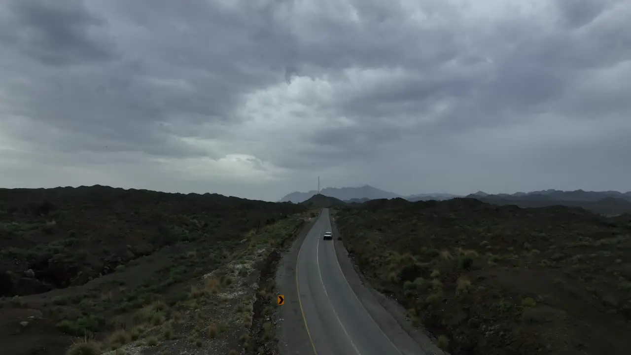 Aerial drone shot of a highway with a vehicle moving on the road and wast landscape and dark clouds on the sky