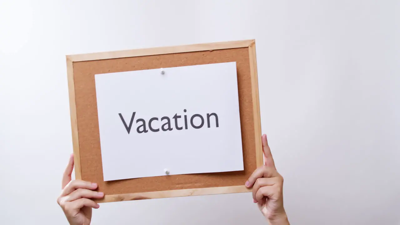 Woman's hand shows the paper on board with the word Vacation in white studio background with copy space