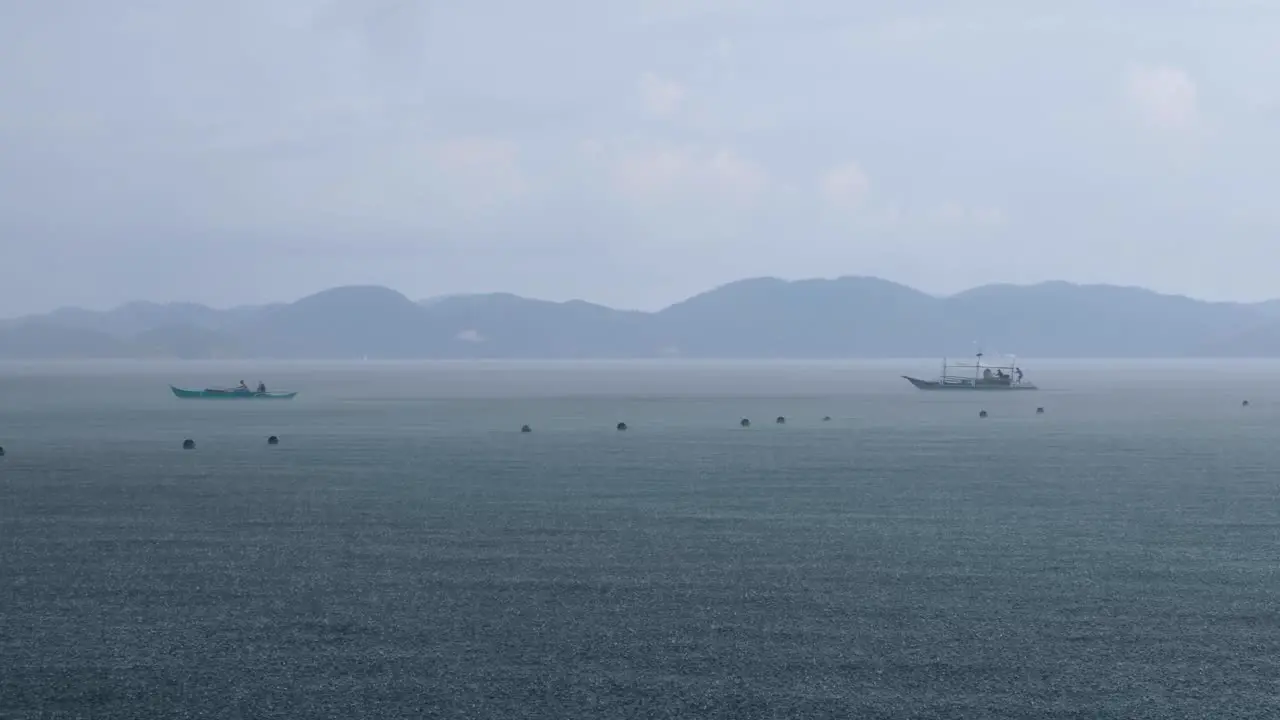 Local fishing and transport boats heading for shelter during rainy downpour and grey cloudy skies in Coron Bay of Palawan Philippines