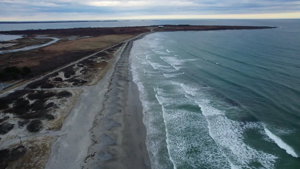 Aerial of ocean waves slowly crashing on a beach on a cloudy day