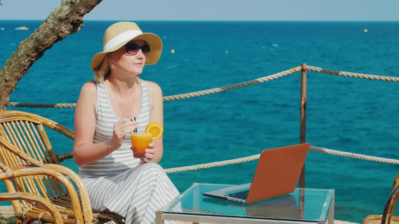 Woman Tourist Relaxing In A Cafe With A View Of The Sea And Drinking Cocktail Nearby Is A Laptop On 