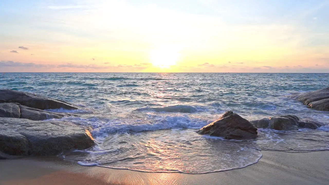 Ocean waves reflecting the colors of a tropical sunset as they roll into shore over large rocks