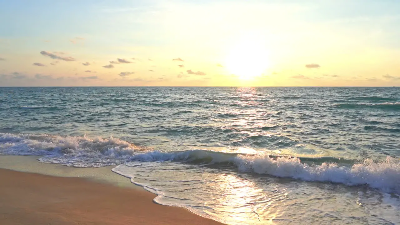 Waves crashing on a sandy beach reflect the colors of a tropical sunset