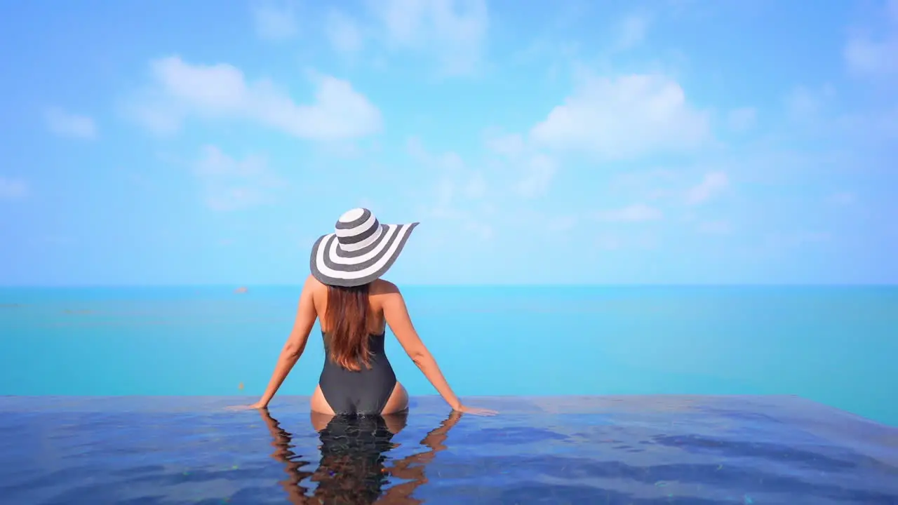 A healthy fit woman sits on the edge of an infinity-edge pool that overlooks the ocean horizon