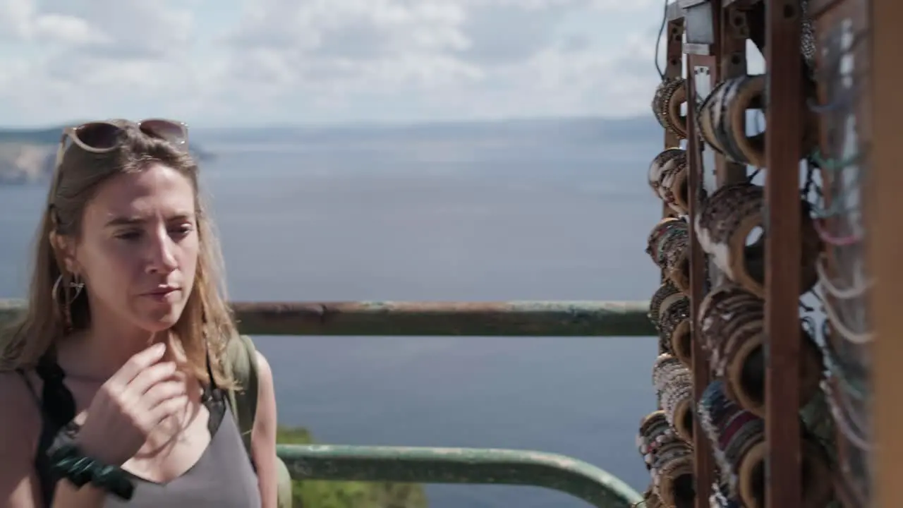 Young woman with backlight at a craft kiosk buying bracelets with the ocean in the background