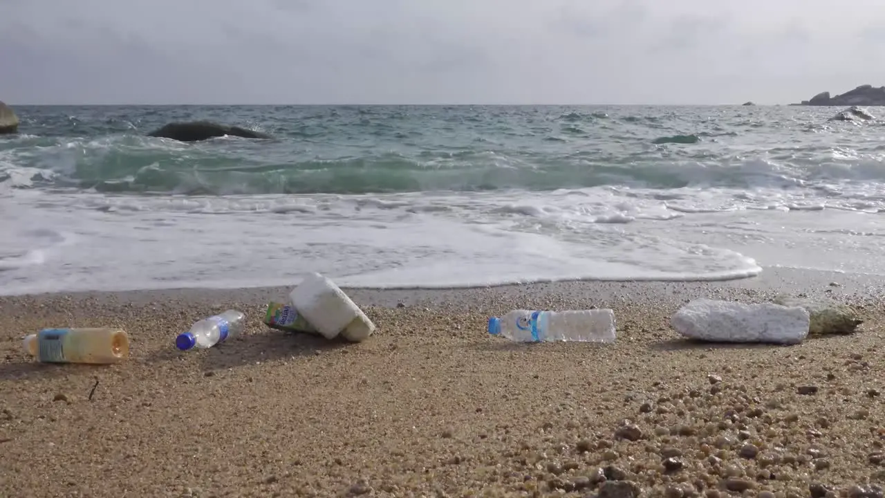 Rushing wave pushing up plastic trash to the beach Low angle parallel static 4K side shot