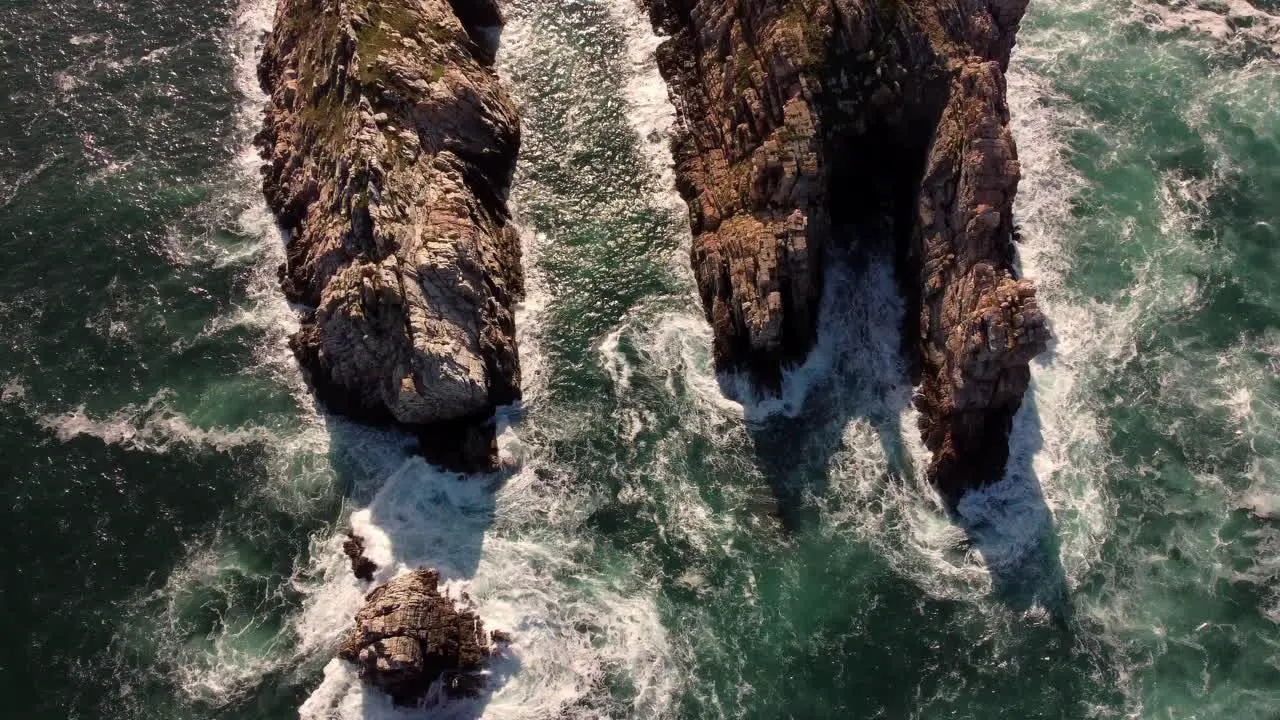 Aerial top view of waves breaking on rocks in a blue ocean