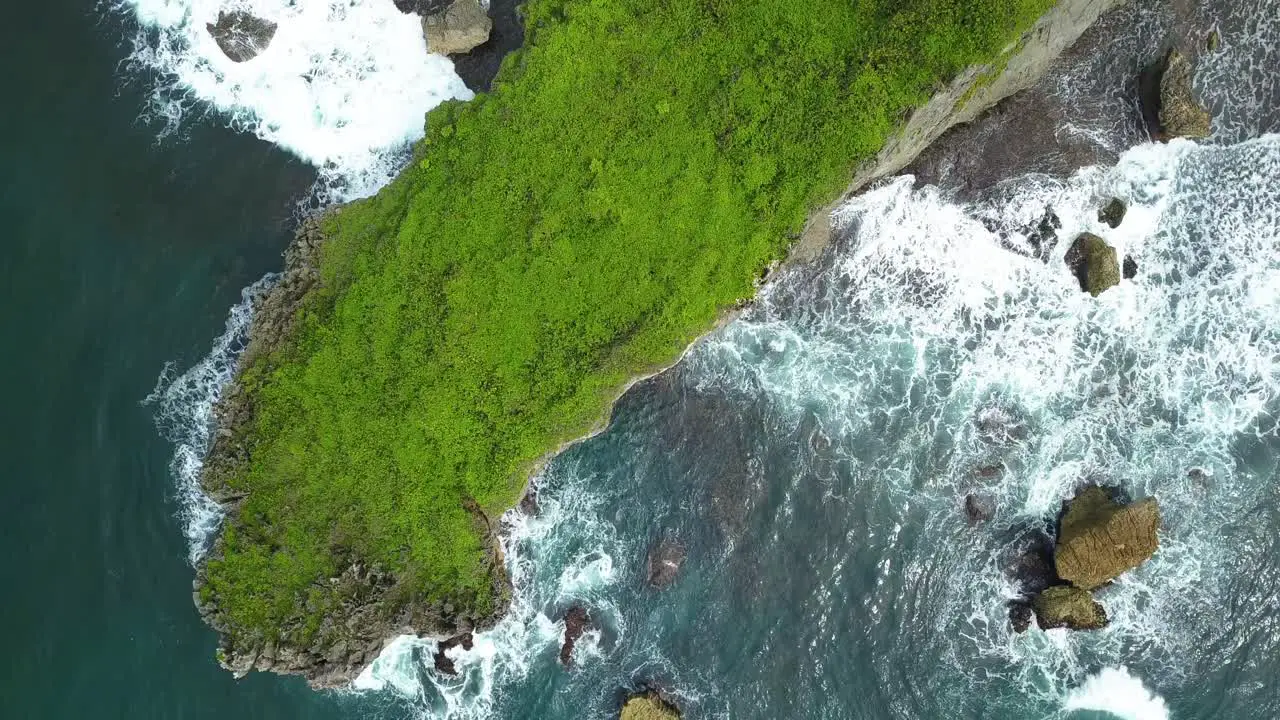 Aerial view of lush green cliffs and waves crashing on coral rock shore