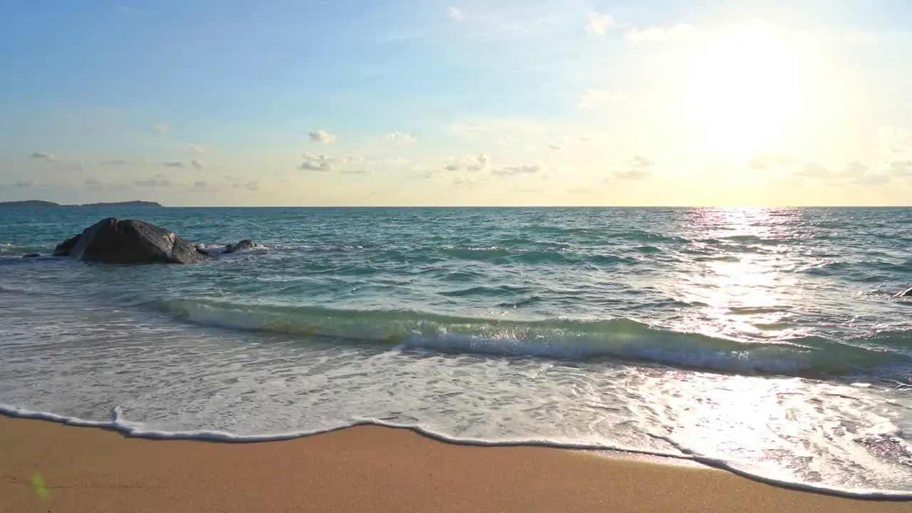 Waves roll in on a tropical beach as the sun sinks in the western sky