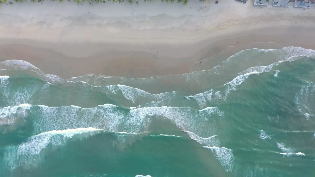 Ocean waves crashing into white sand beach filmed from above by drone