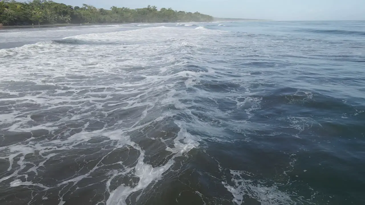 AERIAL Camera follows deep blue ocean waves into island with green forest jungle