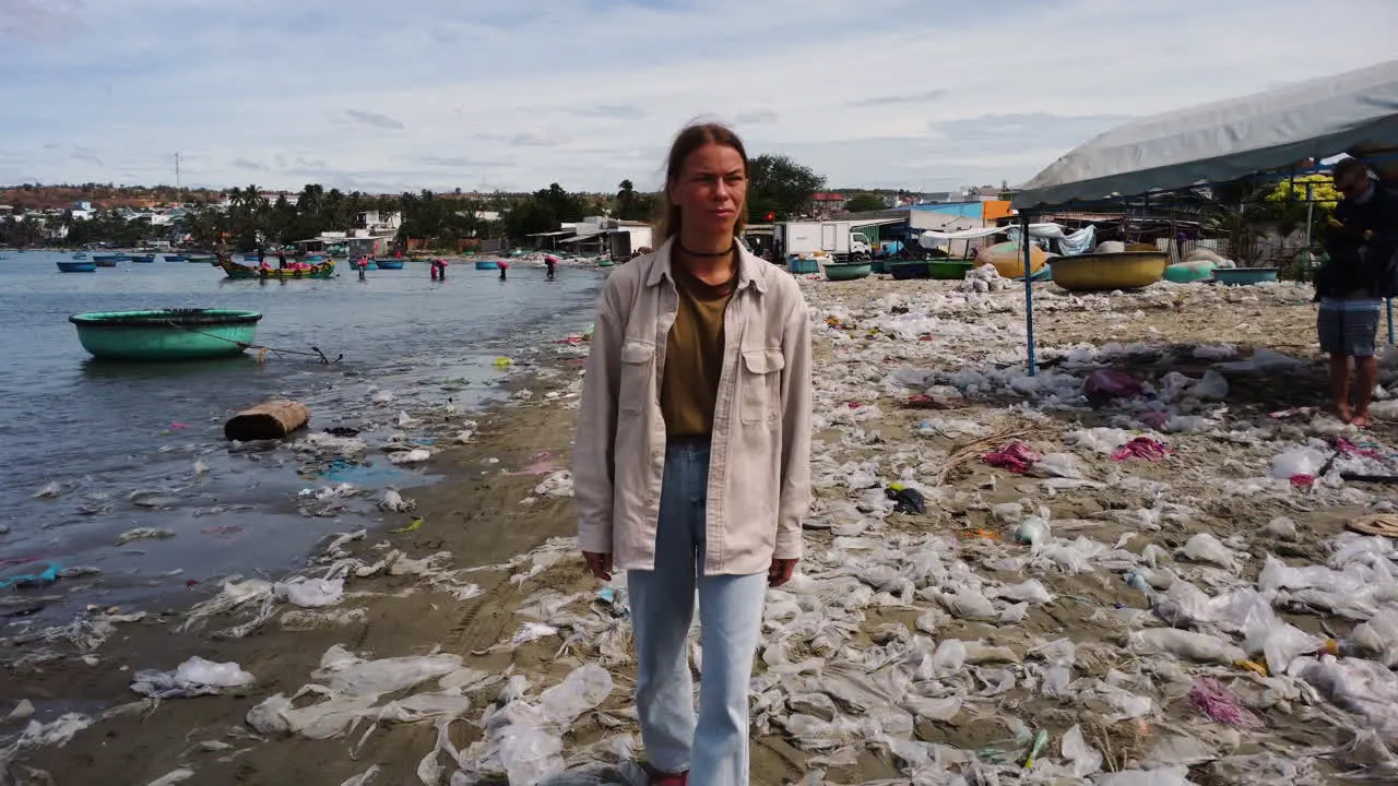 Young caucasian woman wearing eco friendly sustainable clothings walking barefoot sandals on tropical beach with plastic waste garbage pollution