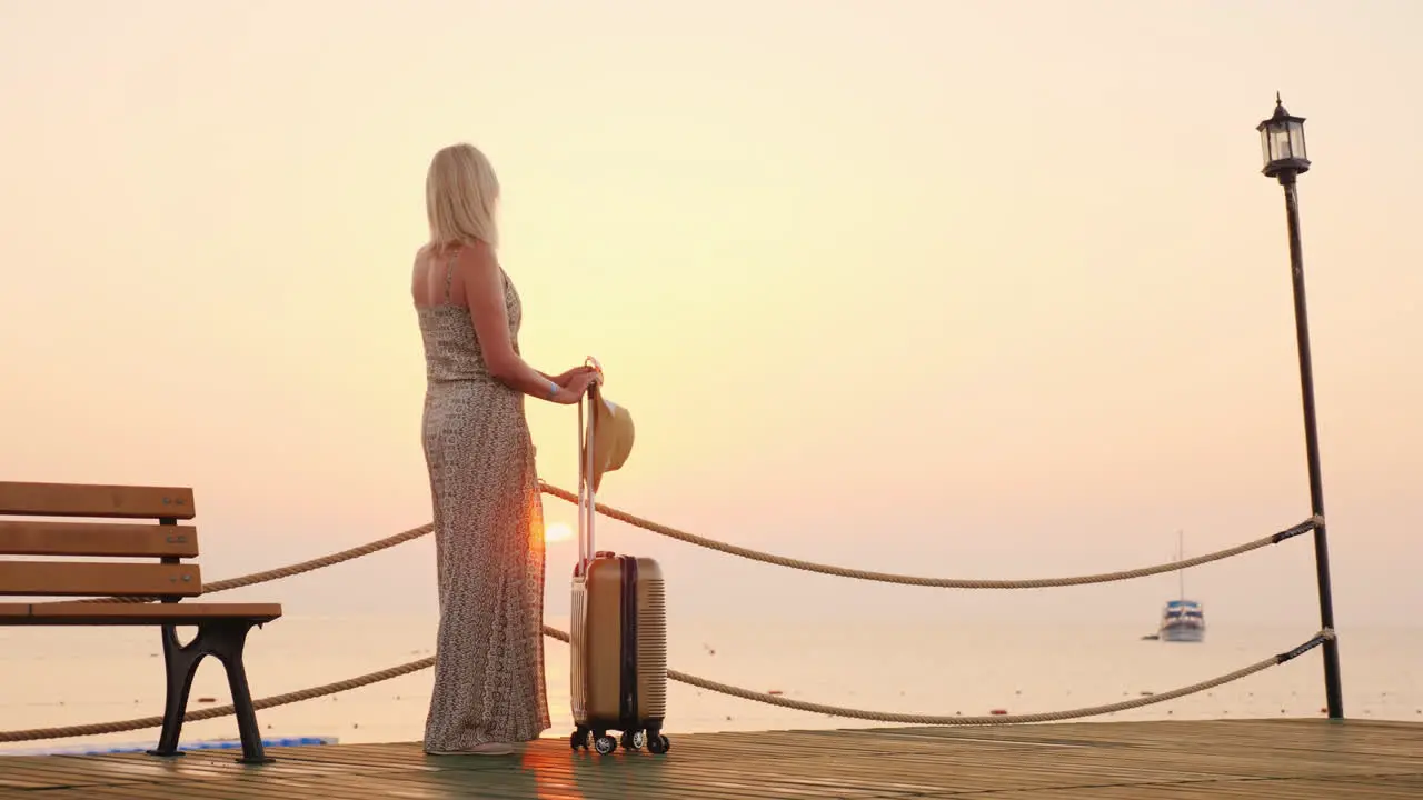 A Young Girl In A Summer Sundress Expects To Settle In A Resort Hotel Stands With A Suitcase On The 