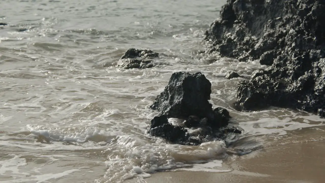 Waves on sandy beach from ocean crashing against black volcanic rocks