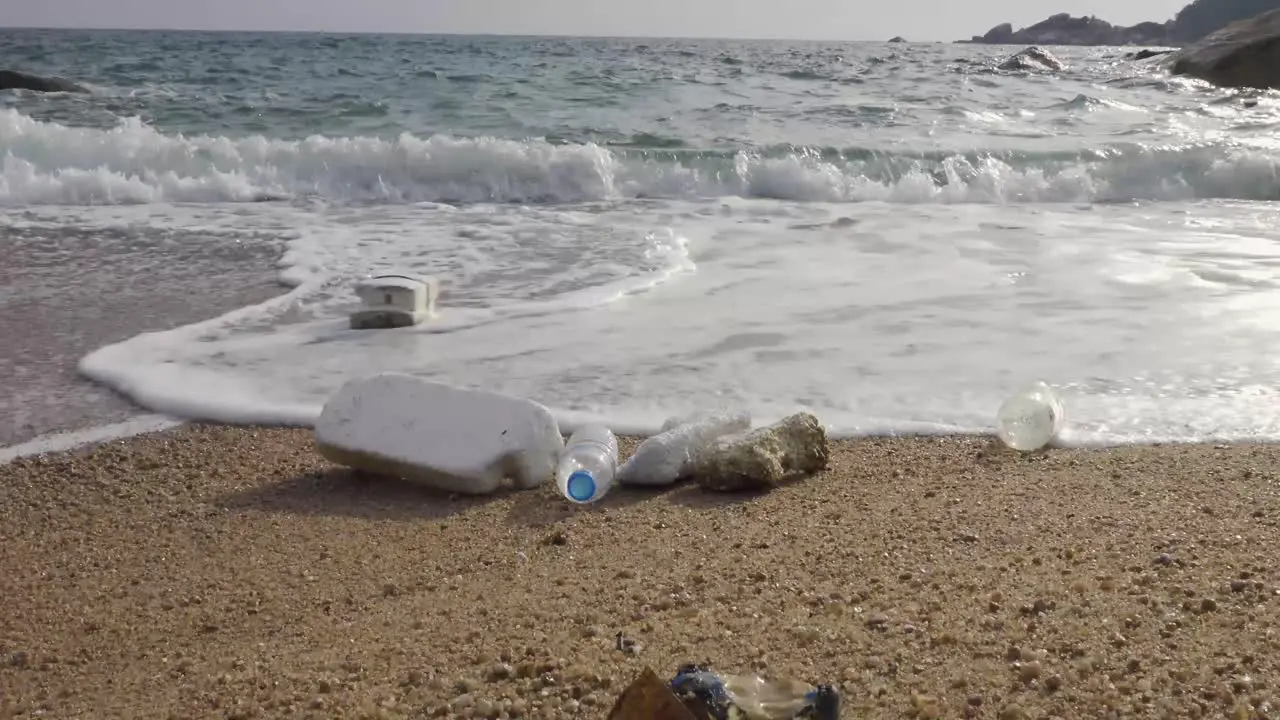 Hush wave washing over plastic trash on the beach Low angle parallel static 4K front shot