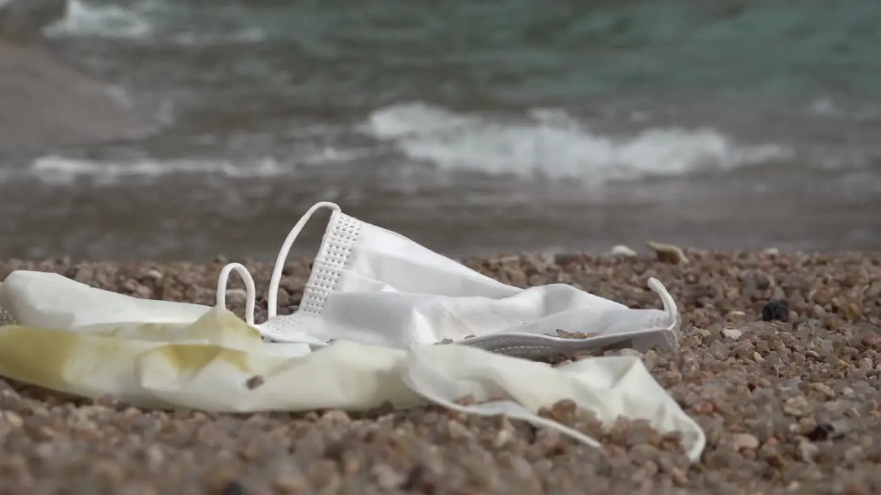 Discarded mask and glove on a beach with continuous rushing wave nearby steady shot moving right