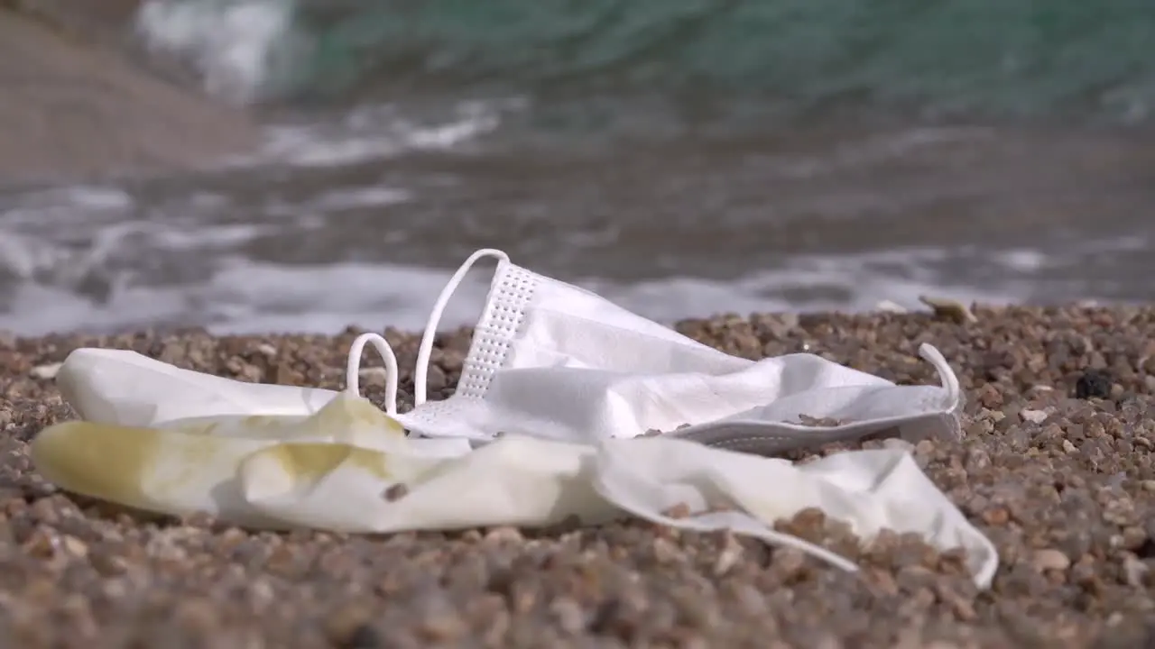 Discarded mask and glove on a beach with continuous rushing wave nearby steady shot moving left