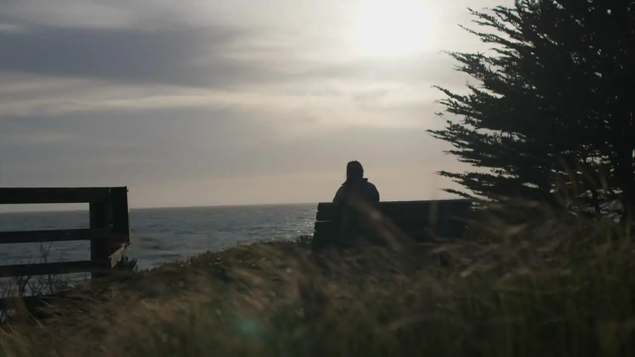 Person sitting on bench by ocean cliff looking out to sea