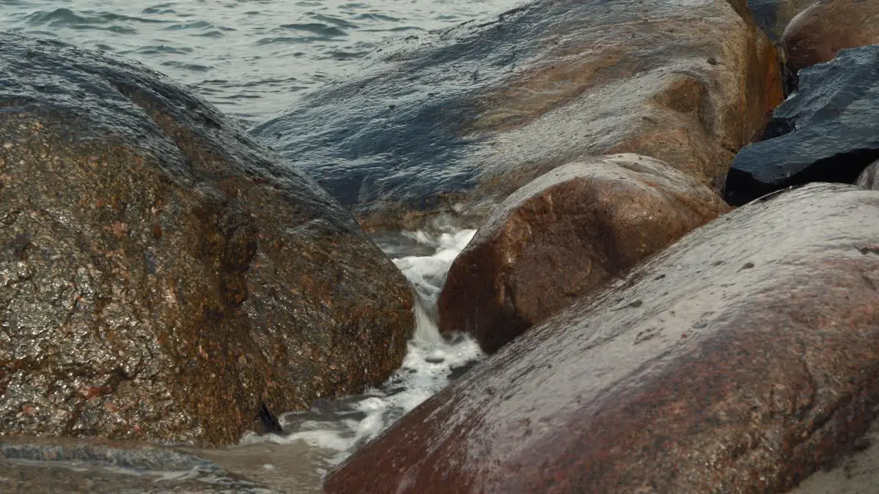 Waves rolling and crashing into stones on overcast day narrow view