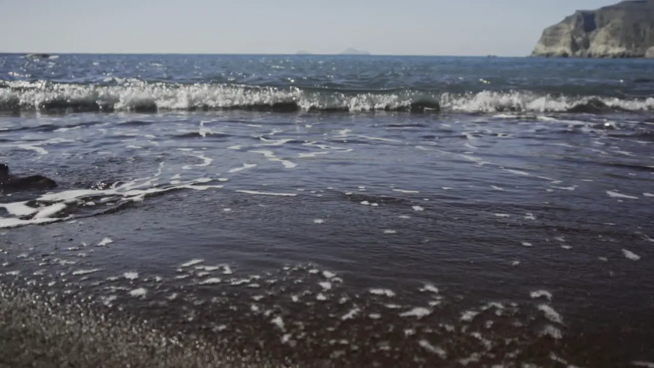 Slow motion shot of waves rolling onto black sand beach on bright day