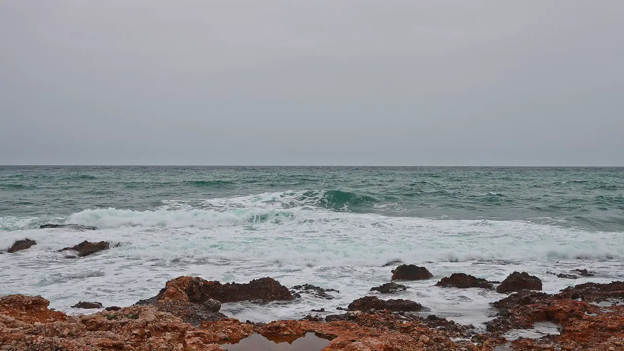 Ocean in a bad weather day gray sky blue waves crashing into orange rocks of the coastline