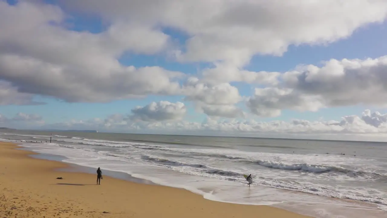 A lone surfer stands watching the waves beach and partly cloudy sky in the background