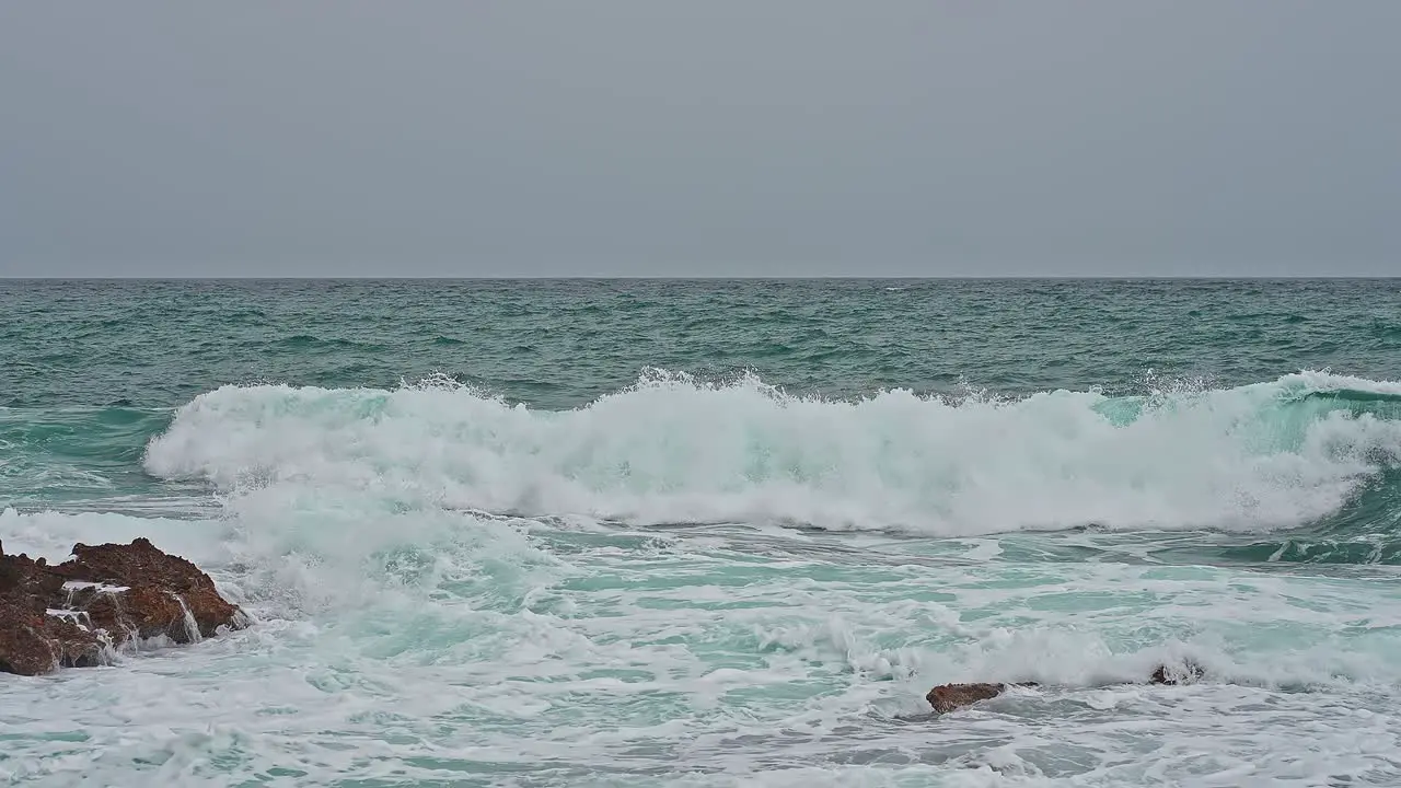 Coast in a bad weather day gray sky blue big waves crashing into orange rocks of the coastline