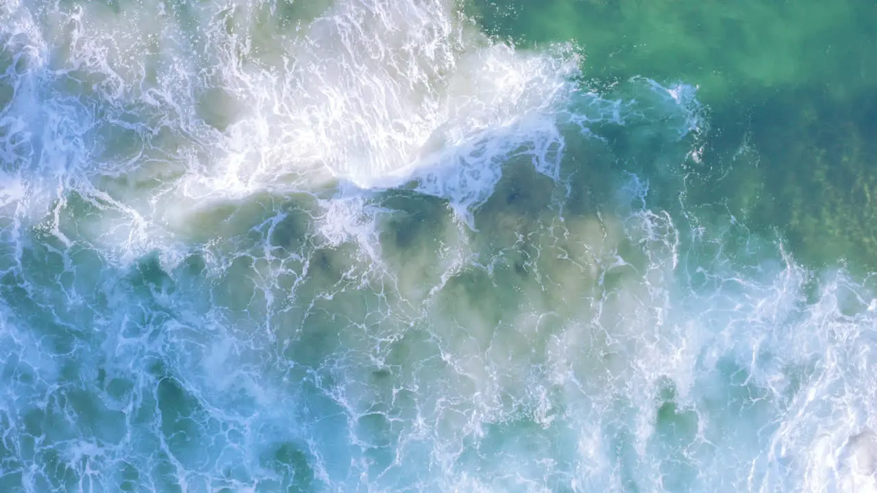 White fringed waves rolling in from top of screen onto shallow sandy coastline Tamarama beach Sydney Australia POV drone