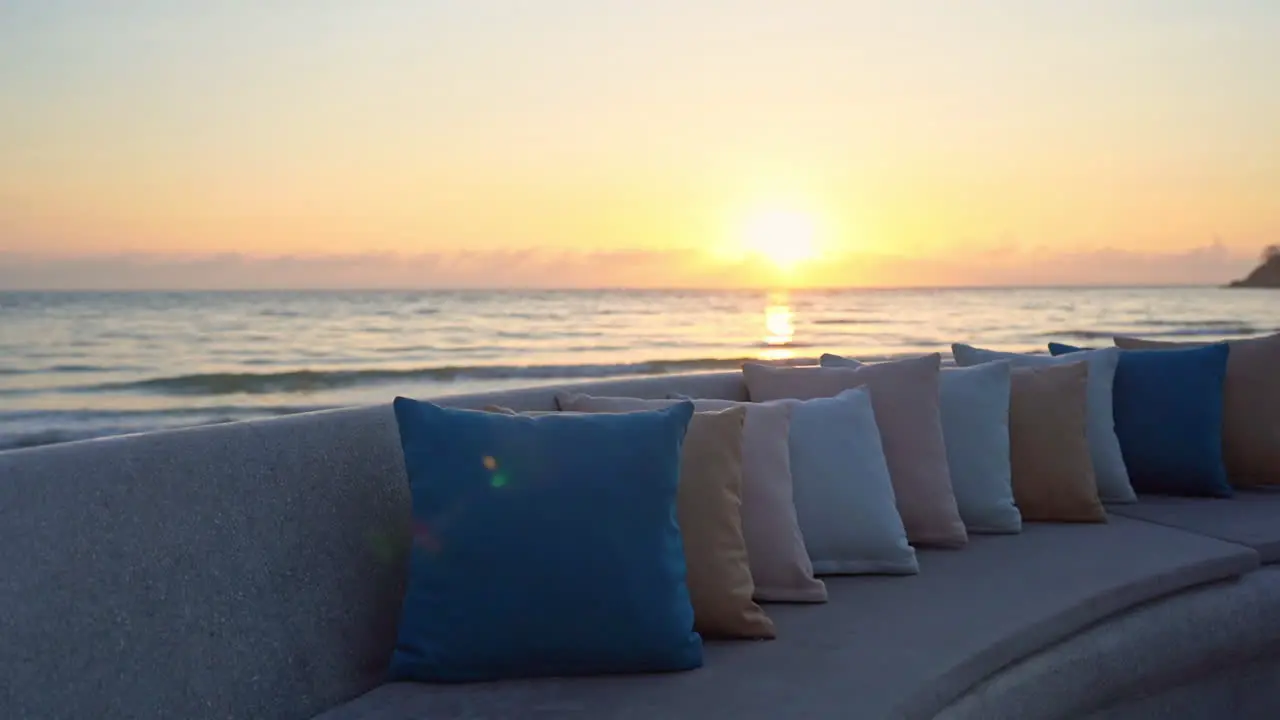 A seaside couch lined with colorful pillows waits for a passing tourist to sit and enjoy the sun setting into the ocean horizon