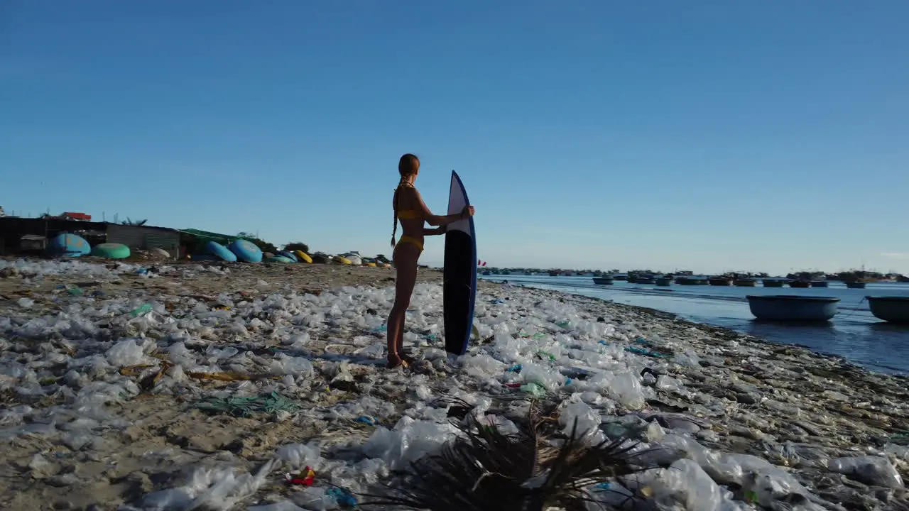 Caucasian young athletic female surfer stand in polluted beach with plastic waste trash garbage Mother Earth ocean pollution save the planet concept