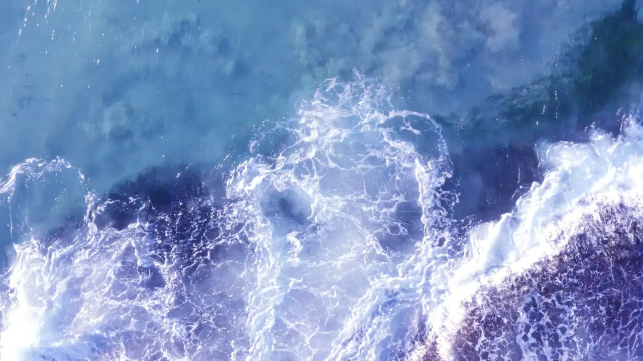 White fringed waves crashing in from top of screen onto ocean rocks Tamarama Beach Sydney Australia POV drone directly above and pan right then pull away