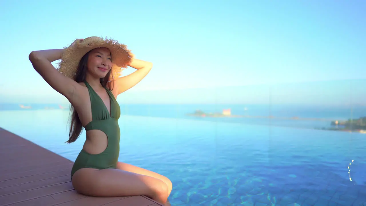 A beautiful Asian woman sitting by an infinity pool at a luxury spa and hotel resort