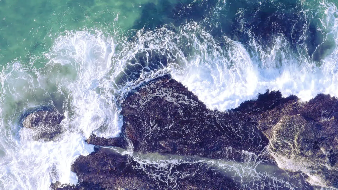 White fringed waves crashing in from top of screen onto sea rocks Tamarama Beach Sydney Australia POV drone directly above