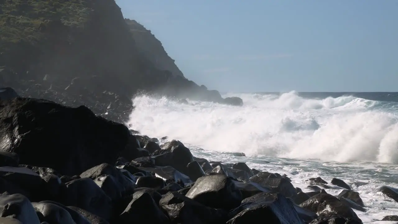 Big waves rolling and crashing into rocky coast on sunny day