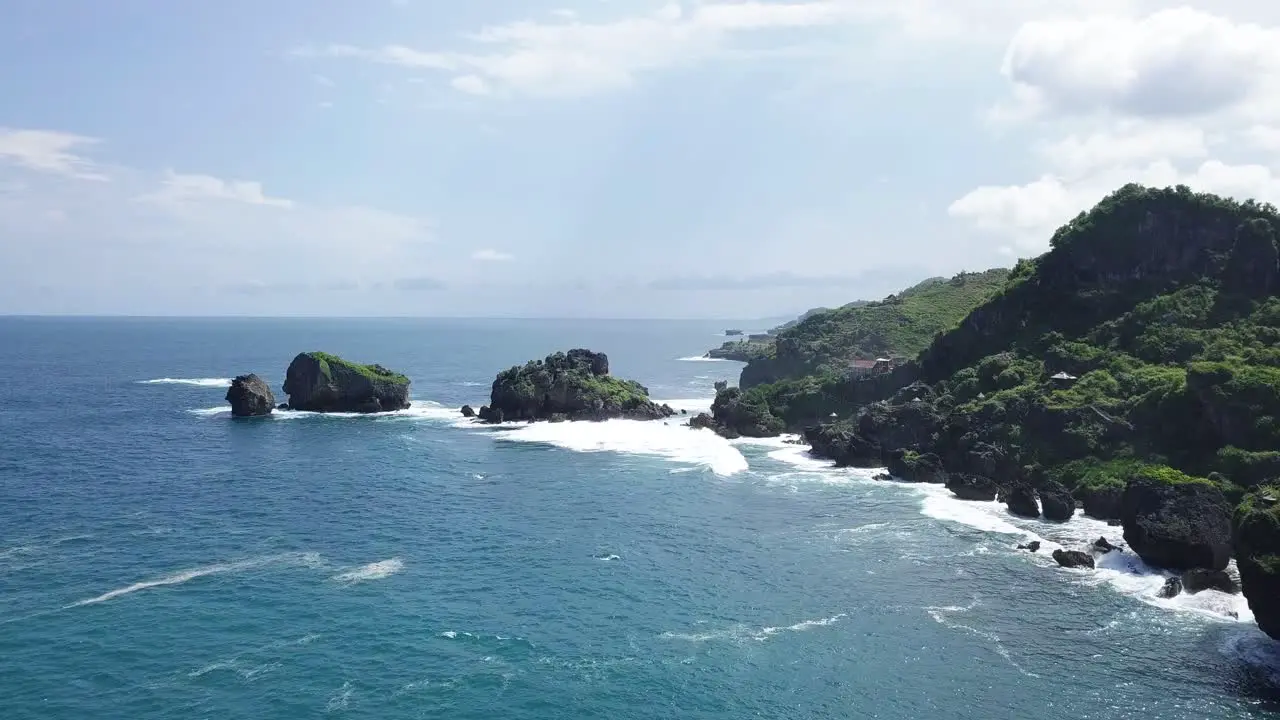 Drone shot of cliff with rocky island on the beach hit by waves during sunny day TIMANG ISLAND YOGYAKARTA INDONESIA