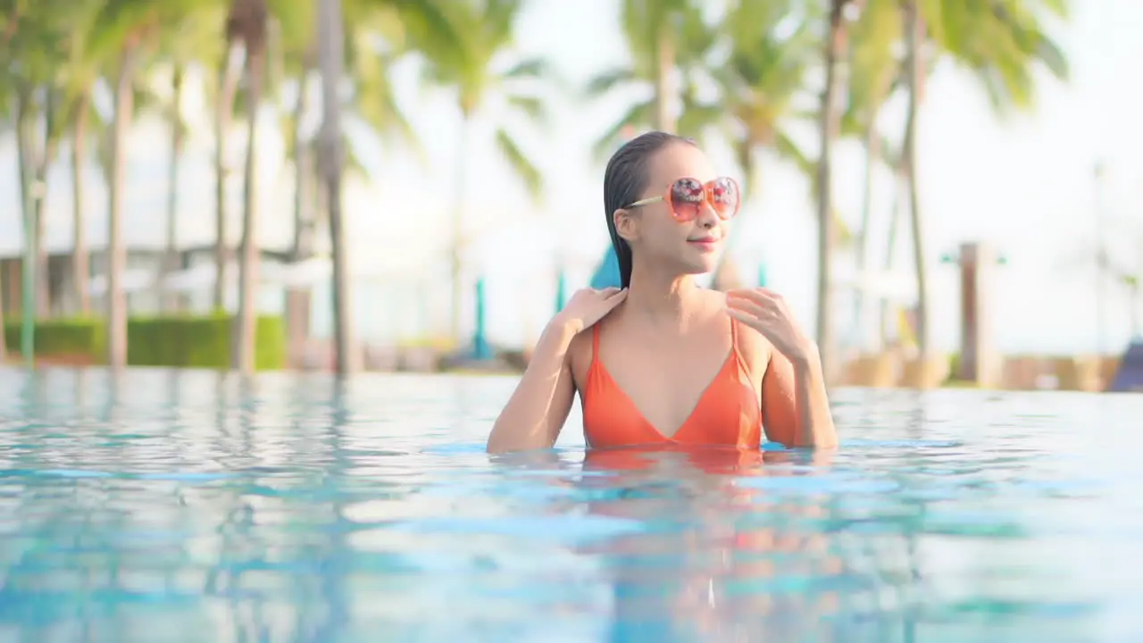 Sexy asian woman on tropical vacation caresses wet hair in swimming pool on hot summer day slow motion