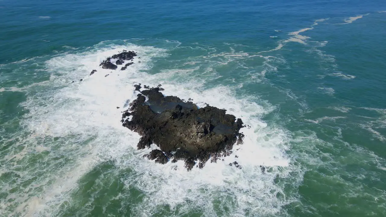 Aerial top view showing foam of breaking waves against coral rock in sunlight