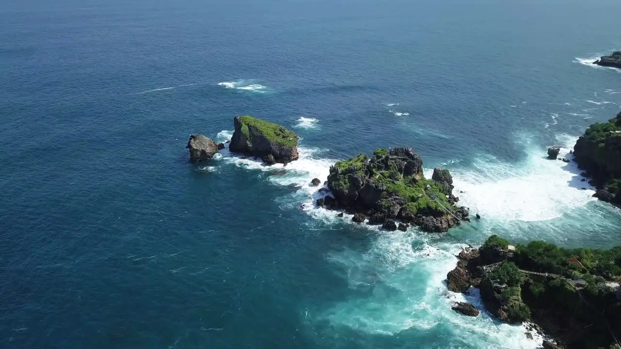 Aerial view showing blue colored ocean waves crashing against coral rocks at Timang Island Indonesia